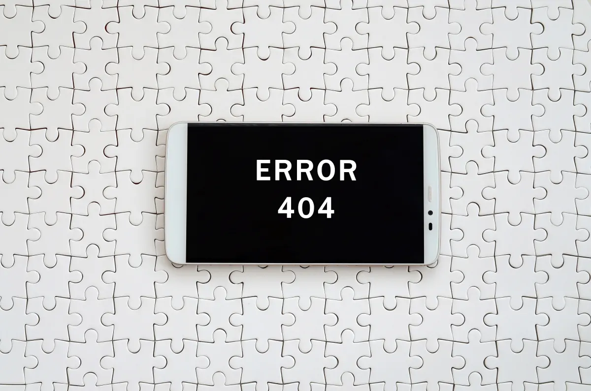 A white smartphone displaying "ERROR 404" on its black screen, resting on a background of white jigsaw pieces.