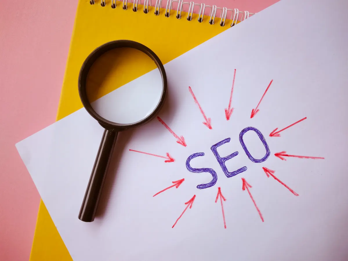 Magnifying glass over a paper with "SEO" encircled by red arrows, symbolizing search engine optimization analysis and focus.